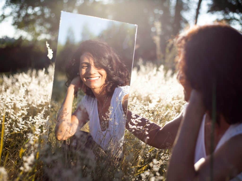 Une femme se regarde dans un miroir assise dans un champ